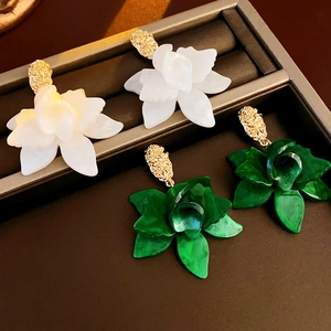 Detail view of large white and green camellia earrings with gold texture in a jewelry box