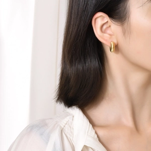 Golden hollow croissant earrings in titanium steel worn by a model on plain background