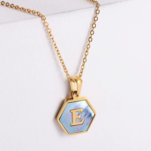 Macro view of gold hexagonal pendant necklace with blue mother of pearl inlay and letter E