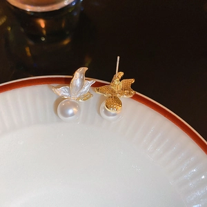 Macro view of gold butterfly earrings with white pearls on a white porcelain dish