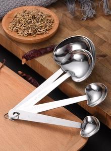 Close-up of heart-shaped stainless steel measuring spoons on a rustic wooden board