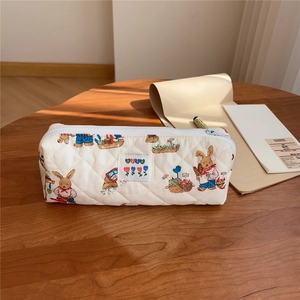 Close-up of quilted beige pencil case with vintage rabbit print on a wooden desk