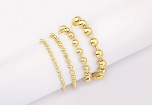 Detail of four sizes of 18k gold plated ball chain bracelets on white cylinder