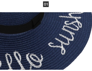 Close-up of navy straw sun hat featuring white embroidered text on the wide brim