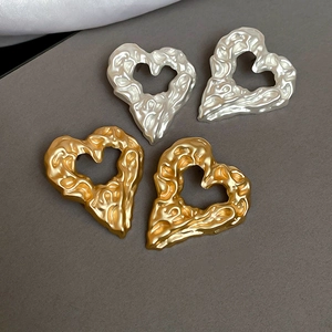 Detail of gold and silver heart earrings with melting lava texture on grey display
