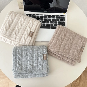 Detail of cable knit wool scarves in beige, grey and camel with logo patches