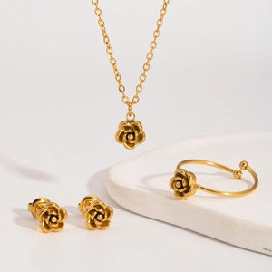 Detailed view of golden rose jewelry set including necklace, earrings, and ring on white plate