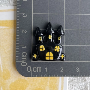 Detailed view of a black resin castle charm with yellow windows measured on a scale mat