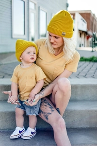 Detail of yellow knit beanie with brand label paired with mustard yellow pocket T-shirt