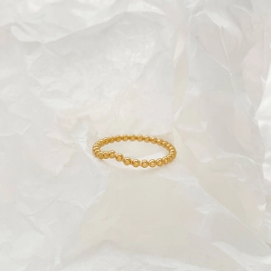 Macro detail of a V-shaped golden beaded ring on a minimalist white textured paper