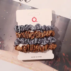 Set of 4 satin scrunchies in light grey and gold brown colors on a white display card
