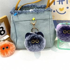 Dettaglio di portachiavi a forma di gatto di peluche grigio e arancione su borsa in denim