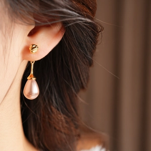 Close-up of elegant gold lava texture stud with a pink teardrop pearl earring on model