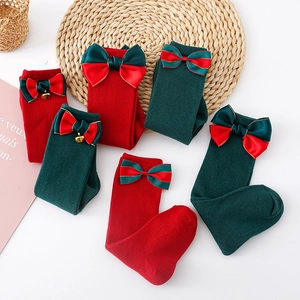 Detail of Christmas knee high socks with satin bows and golden bells on knit fabric