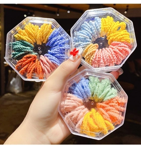 Three hexagonal boxes of small colorful hair elastics held in hand with macro focus