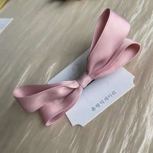 Close-up of a pink bow hair clip made of textured ribbon on a white card display