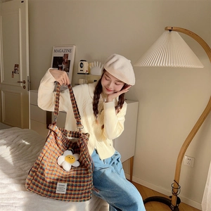 Detail of colorful plaid tweed tote bag featuring white floral pendant and textured fabric