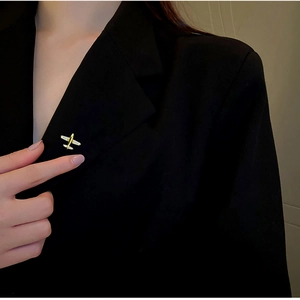 Detail of a minimalist gold airplane brooch pinned on a black suit jacket lapel