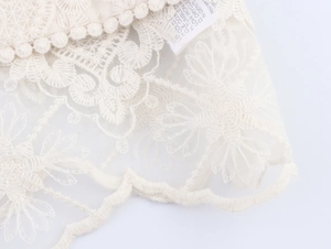 Dettaglio ricamo in pizzo floreale bianco con frange a pompon ed etichetta di cura