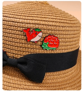 Detailed close-up of cute strawberry whale and hedgehog enamel pins on a straw hat