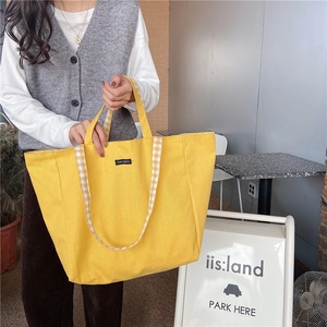 Detail of yellow canvas tote bag featuring contrast plaid handles and merciparis label