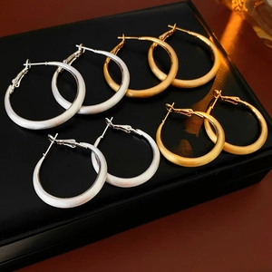 Detailed view of matte gold and silver geometric hoop earrings on black leather base