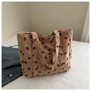 Close-up of beige corduroy tote bag featuring red strawberry patterns and wide handles
