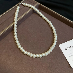 Detailed top-view of a minimalist white beaded pearl necklace on a dark display tray