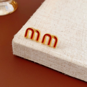 Close-up of gold-plated red enamel letter earrings on a beige linen jewelry display