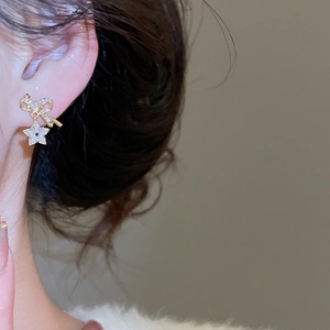 Close-up of a model wearing elegant gold bow and star drop earrings with sparkling zircons
