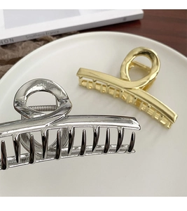 Detail showing gold and silver wide metal shark hair clips on a white ceramic plate