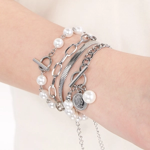 Close-up of layered silver flat snake and pearl bead bracelet with coin pendant