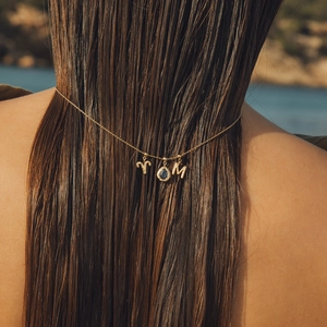 Close-up of gold necklace with blue birthstone and initials worn on back at the beach