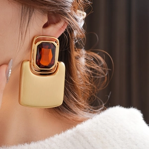 Close-up of golden rectangular earrings with brown gemstones worn by a model