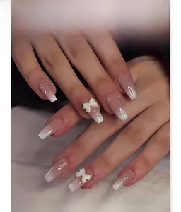 Close-up of pink and white ombre ballerina press-on nails with 3D white bow charms