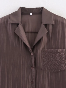 Detail of chocolate brown pleated silk shirt featuring embroidered pocket and buttons