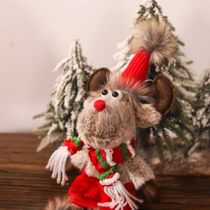 Detail of plush reindeer doll with a red knit hat and striped scarf in a snowy scene