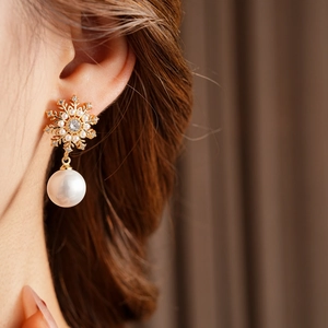 Gros plan de boucles d'oreilles flocon dorées avec perles et zircon sur l'oreille