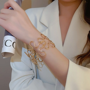 Detail of a wavy gold open cuff bracelet on a model wearing a white formal blazer