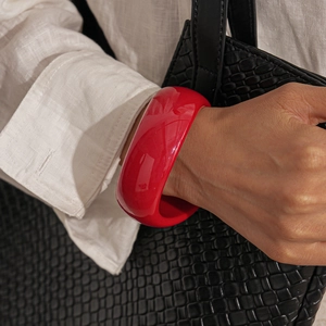 Detail of glossy red acrylic wide bangle bracelet styled with black woven texture background