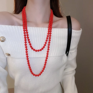 Detail of red faux pearl long layered necklace draped on a white off-shoulder top