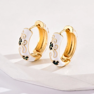 Close-up of golden hoop earrings with white enamel and green floral patterns