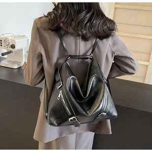 Detail of a black glossy leather triangular backpack with silver metal zippers on back