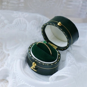 Close-up of a slim gold ring with a green gemstone inside a luxury green velvet box
