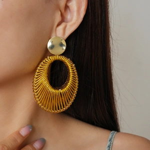 Detail of a model wearing a gold velvet woven hollow oval earring with metallic texture