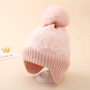 Close-up of pink knit winter hat with white jacquard patterns and a large fluffy pom-pom
