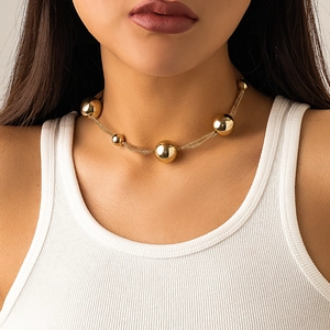 Detail shot of a layered gold choker necklace with large metallic beads on a model