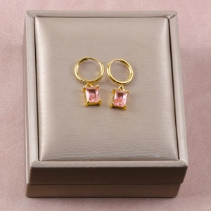 Detalle de pendientes dorados con gemas rosas rectangulares sobre joyero color beige