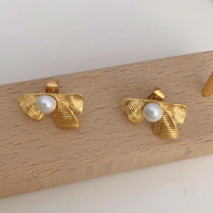Detailed view of gold bow pearl earrings featuring a brushed metal texture on wooden stand