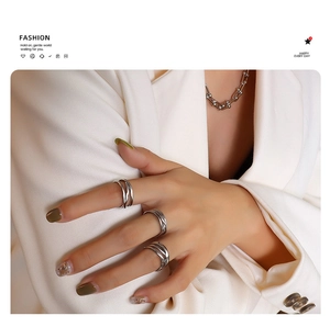 Close-up of three silver layered crossover rings worn on a hand with fashion text